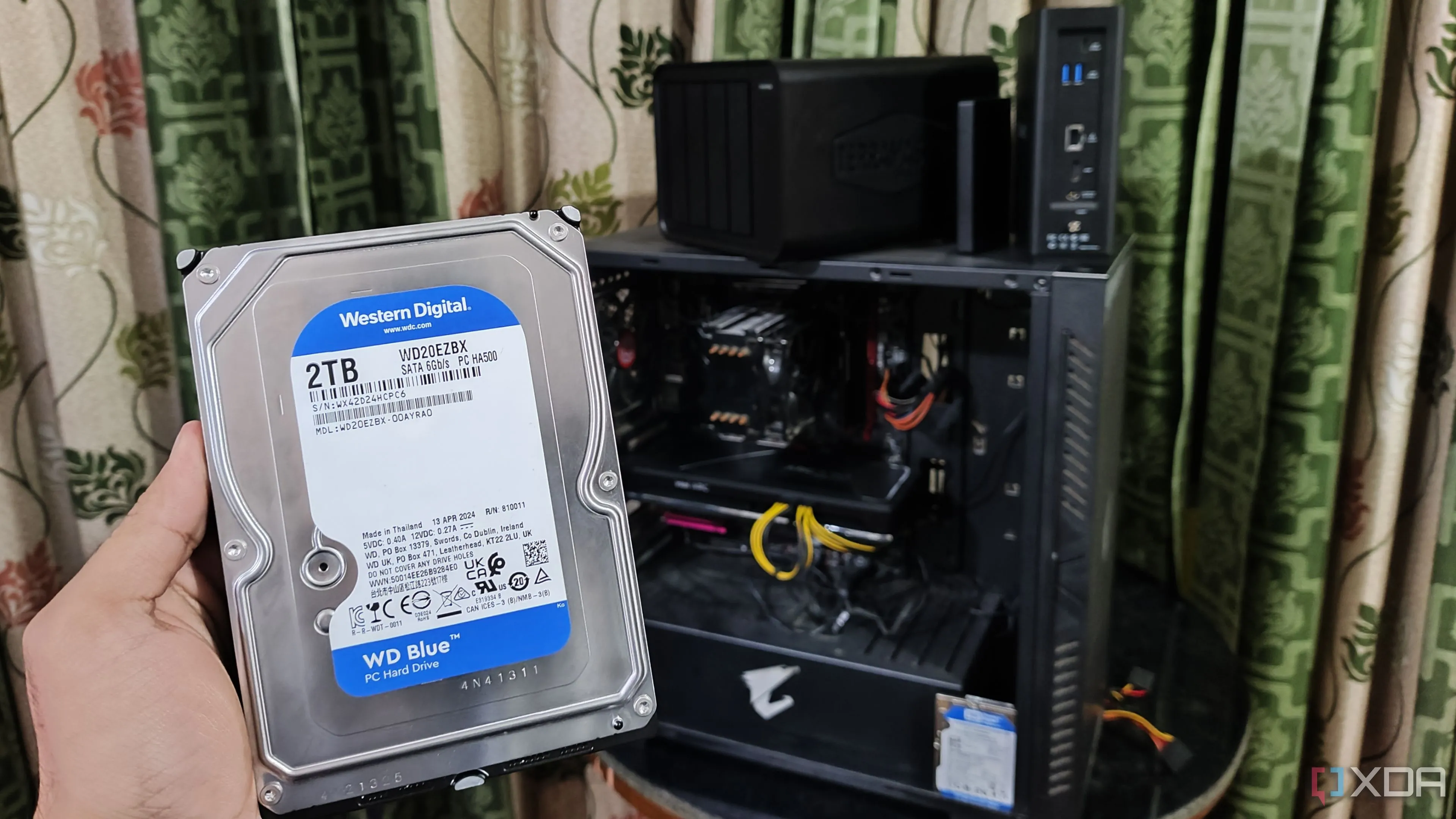 Người cầm ổ cứng HDD trước máy tính PC và hai thiết bị NAS TerraMaster, minh họa cho giải pháp mở rộng bộ nhớ bằng NAS