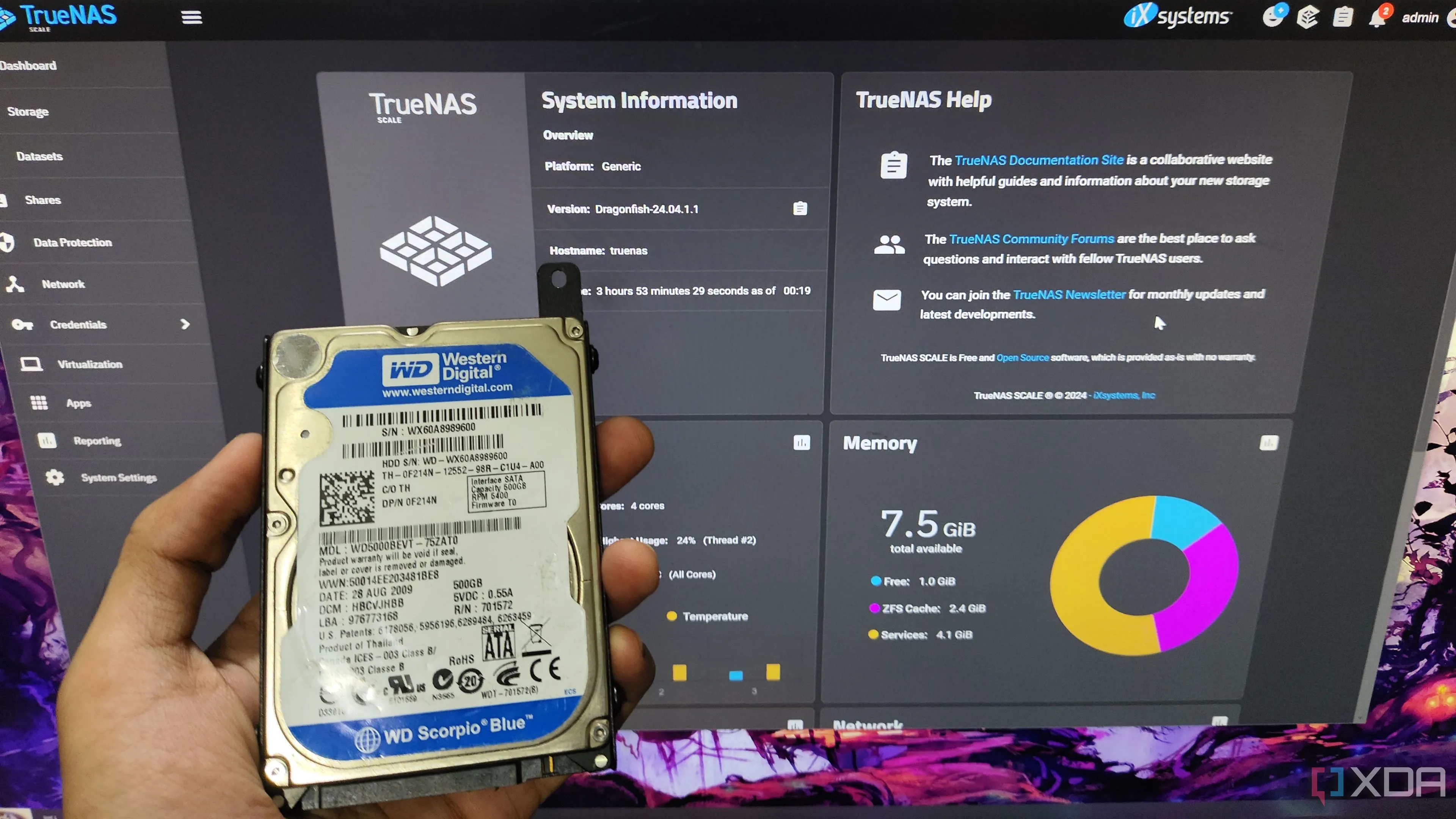 Người dùng cầm ổ cứng HDD trước màn hình giao diện TrueNAS Scale